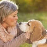 Woman on a grassy field petting and kissing her Beagle pup.